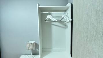 Een klein, wit nachtkastje met een lamp en een dressoir met drie lades en een spiegel.