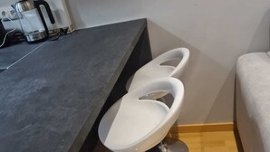 Eine moderne Küche mit dunkler Arbeitsplatte, drei weißen Barhocker und einer Edelstahlspüle.