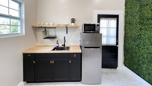 A modern kitchen with a black countertop, a stainless steel refrigerator, and a microwave. There is a window on the left and a green wall on the right. - Modern Ocala Studio Cabin (Ocala)