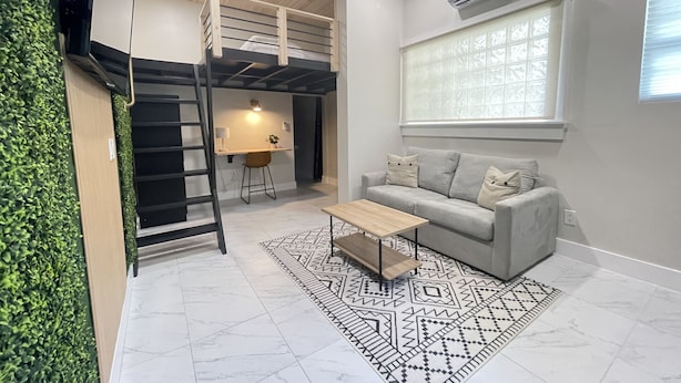A compact living space with a bunk bed, a sofa, a coffee table, a desk with a chair, and a window with blinds. - Modern Ocala Studio Cabin (Ocala)