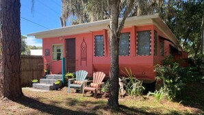 Una casa roja con un porche delantero, dos sillas Adirondack y una valla de madera.