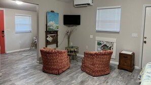 Una habitación con dos sillas de estampado floral, un televisor de pantalla plana, un aire acondicionado y una mesita con un florero.