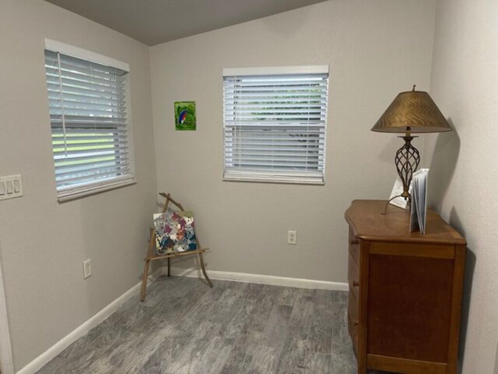 A room with two windows, a small table with a lamp, and a cabinet.