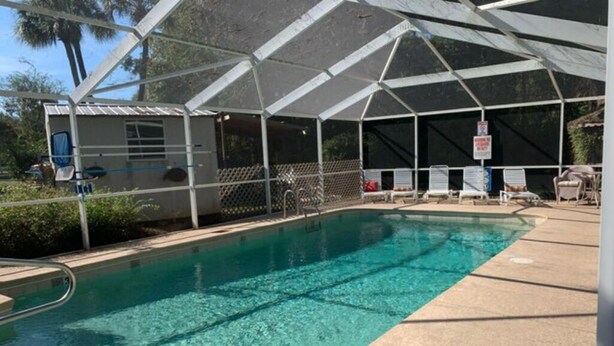 Un área de piscina con una zona de estar cubierta y un pequeño edificio, presumiblemente un vestuario o depósito.