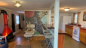 Une cuisine moderne avec des meubles en bois, un four encastré et un coin repas comprenant une chaise blanche et une lampe rouge.