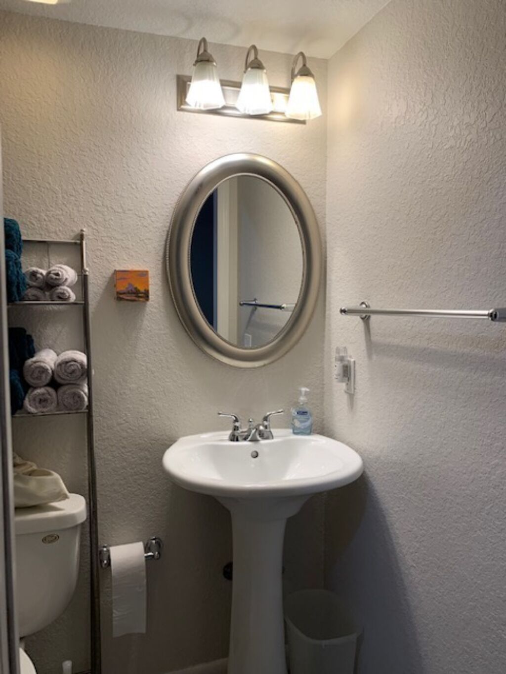 A bathroom with a white sink, a mirror, a towel rack with towels, and a toilet.