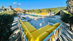 Un área de piscina con sillas reclinables amarillas, una estructura de techo de paja y un cielo azul despejado.