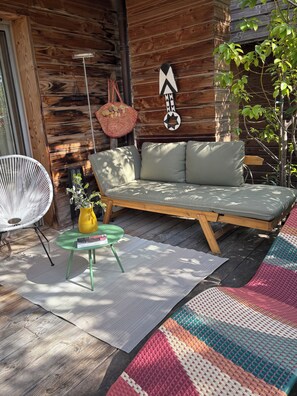 Un espace extérieur accueillant, aménagé avec un canapé, une chaise blanche, une petite table et un tapis coloré en fibres tressées.
