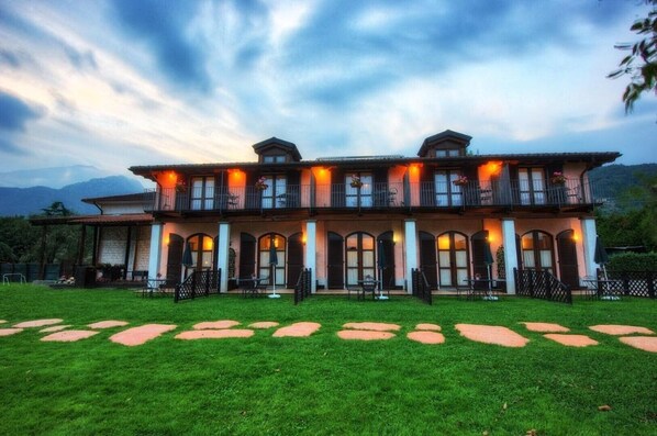 A large, two-story building with a symmetrical facade, multiple balconies, and a well-maintained lawn with stepping stones.