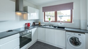 A modern kitchen with white cabinets, a built-in oven, a washing machine, and a window with a view of the outside. - Centrally located, modern & comfortable apartment with parking. (Inverness)