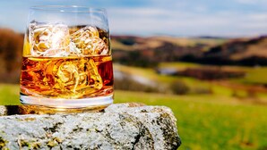 A glass of amber liquid on a stone surface with a blurred landscape in the background. - Centrally located, modern & comfortable apartment with parking. (Inverness)