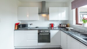 A modern kitchen with white cabinets, a stainless steel range hood, a microwave, a toaster, and a kettle. - Centrally located, modern & comfortable apartment with parking. (Inverness)