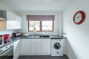 Eine moderne Küche mit weißen Schränken, einer integrierten Waschmaschine, einer roten Uhr und einem Fenster mit Blick nach draußen.