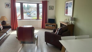 A living room with a sofa, a dining table, a TV, and a window with curtains. - Centrally located, modern & comfortable apartment with parking. (Inverness)