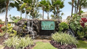 Een tropische tuin met een waterval, palmbomen en een bord waarop 'Kauai' staat.