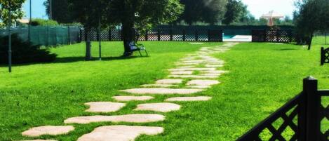 A pathway with stepping stones leading through a well-maintained grassy area, surrounded by trees and a fence.