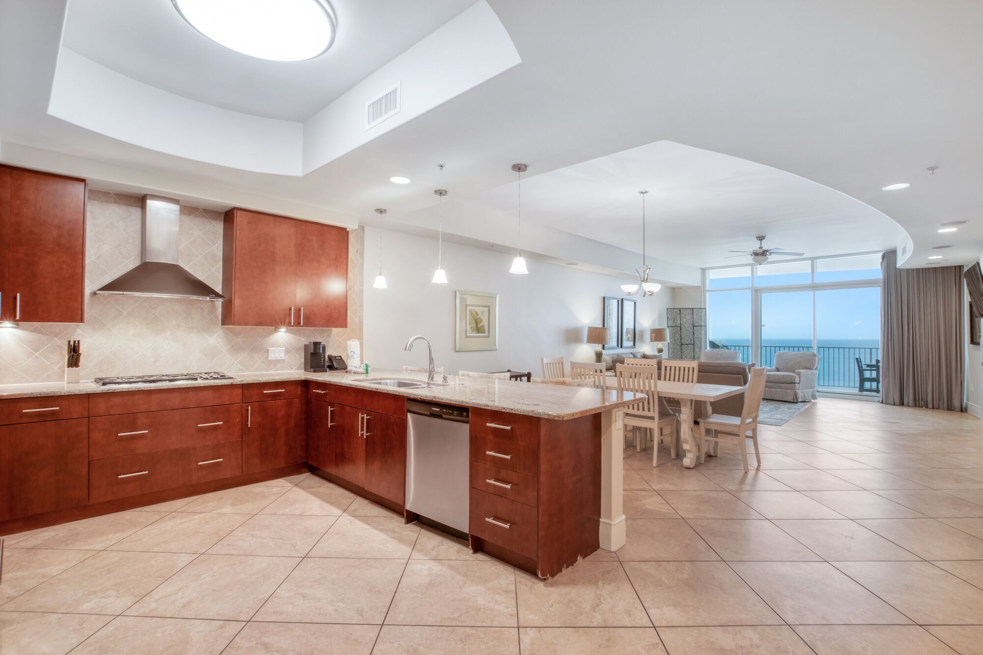 A modern kitchen with a large island, wooden cabinets, and a dining area with a view of the ocean.