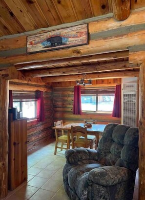 L’intérieur d’une cabane en rondins comprend un coin repas, un canapé et une enseigne au-dessus de la porte.