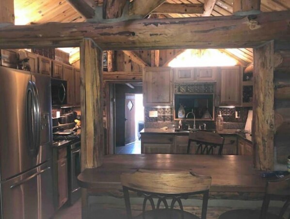 Une cuisine rustique avec des meubles de rangement en bois, un réfrigérateur et une table à manger avec des chaises.