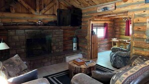 A rustic cabin interior with a stone fireplace, wooden walls, and a cozy seating area. - Fully fenced yard, dogs welcome!  (Lakeside)