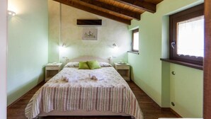 A bedroom with a wooden ceiling, a bed with a striped bedspread, two bedside tables, a window, and a wall-mounted picture. - Agriturismo alla Poncia - Apartment with Garden View (Gravedona)