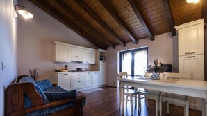 A cozy living room with a wooden sofa and a dining area with a white table and chairs. - Agriturismo alla Poncia - Apartment with Garden View (Gravedona)