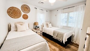 Une chambre avec deux lits, un ventilateur de plafond et une fenêtre avec des rideaux légers.
