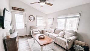 Un salon avec une table basse en bois, un fauteuil à rayures, un canapé beige et un ventilateur de plafond.