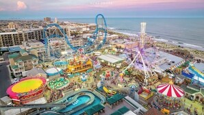 Une vue aérienne d’un parc d’attractions animé, avec des montagnes russes, une grande roue et un toboggan aquatique.
