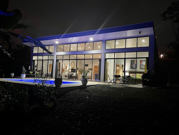 Un bâtiment moderne doté de grandes baies vitrées, d’une piscine et d’un espace extérieur aménagé pour s’asseoir.