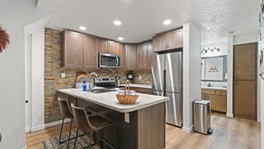 Una cocina moderna con armarios de madera, una isla central con taburetes de bar, un refrigerador de acero inoxidable y un microondas.