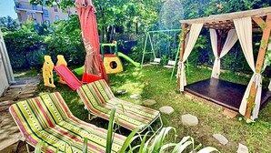 Um jardim com baloiço, parque infantil e área de estar coberta por uma marquise.