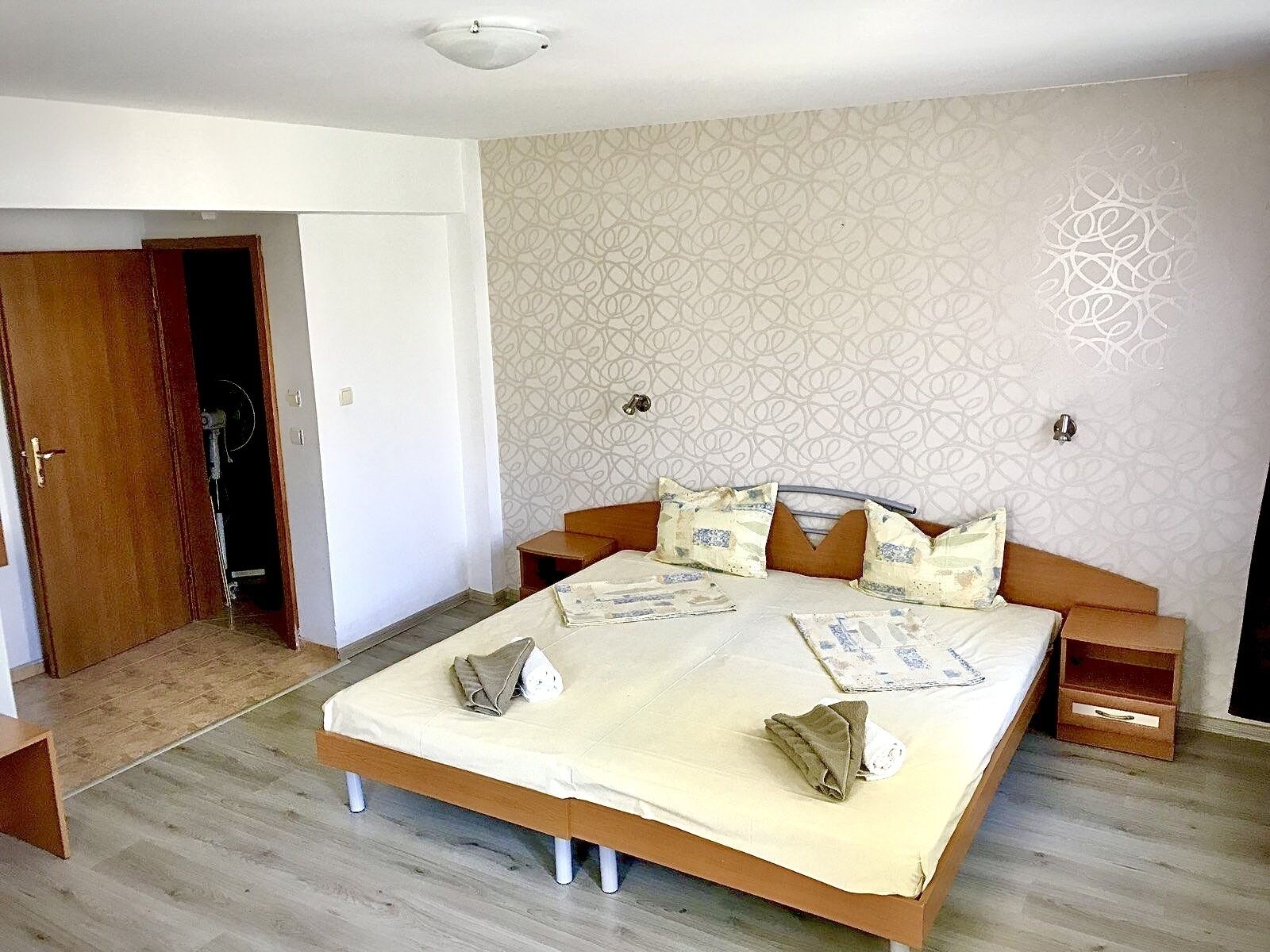 A bedroom with a large bed, wooden headboard, and patterned wallpaper.