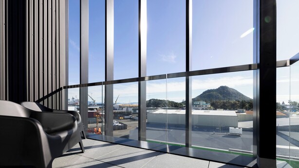 A modern interior with large windows, a black chair, and a view of a mountainous landscape. - Quest Mt Maunganui  (Tauranga)