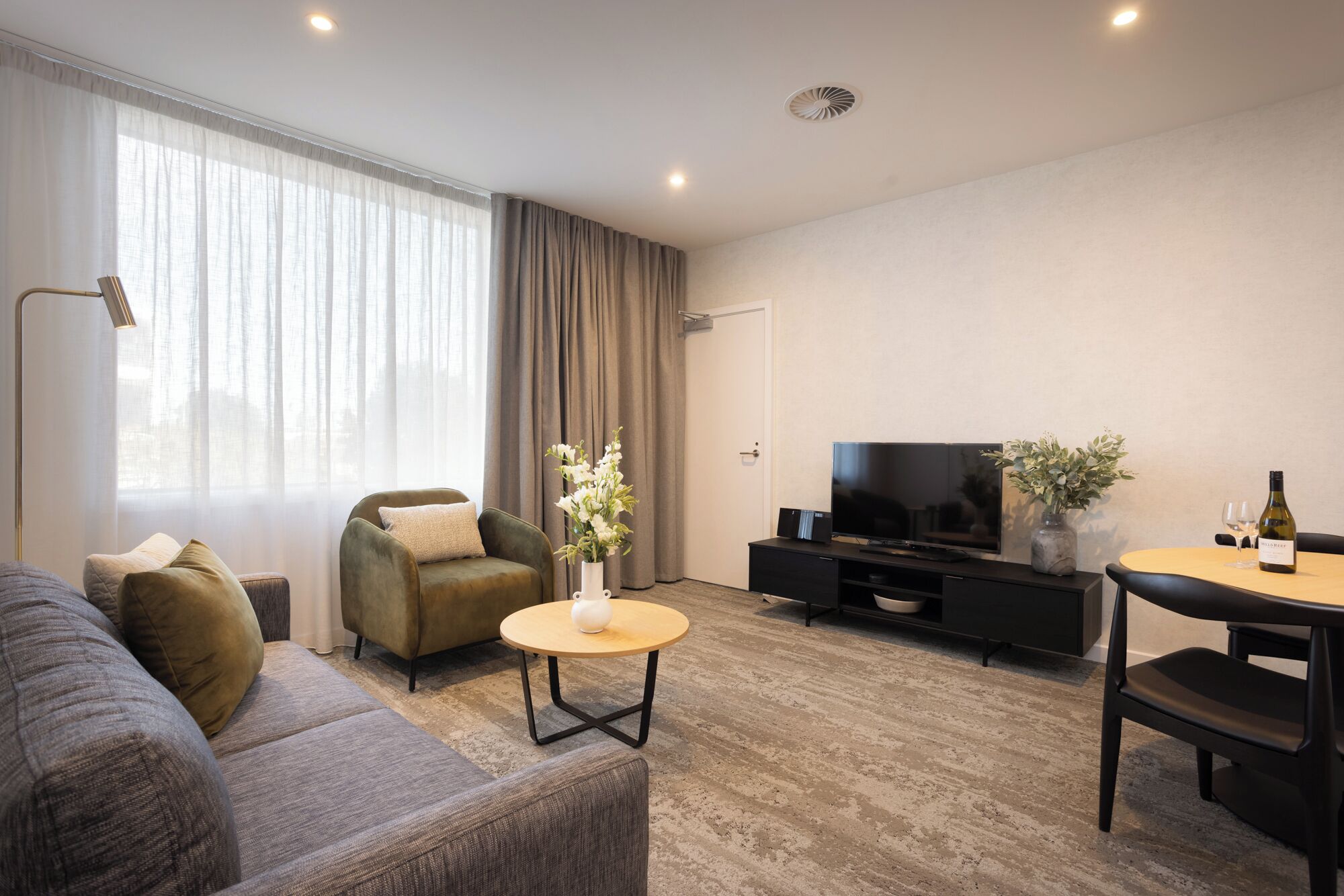 A modern living room with a sofa, armchair, round coffee table, and a TV on a black stand.