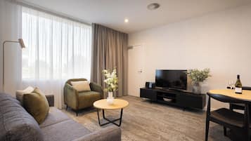 A modern living room with a sofa, armchair, round coffee table, and a TV on a black stand.
