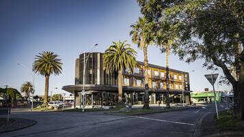 A modern hotel with a curved facade, palm trees, and a clear sky.