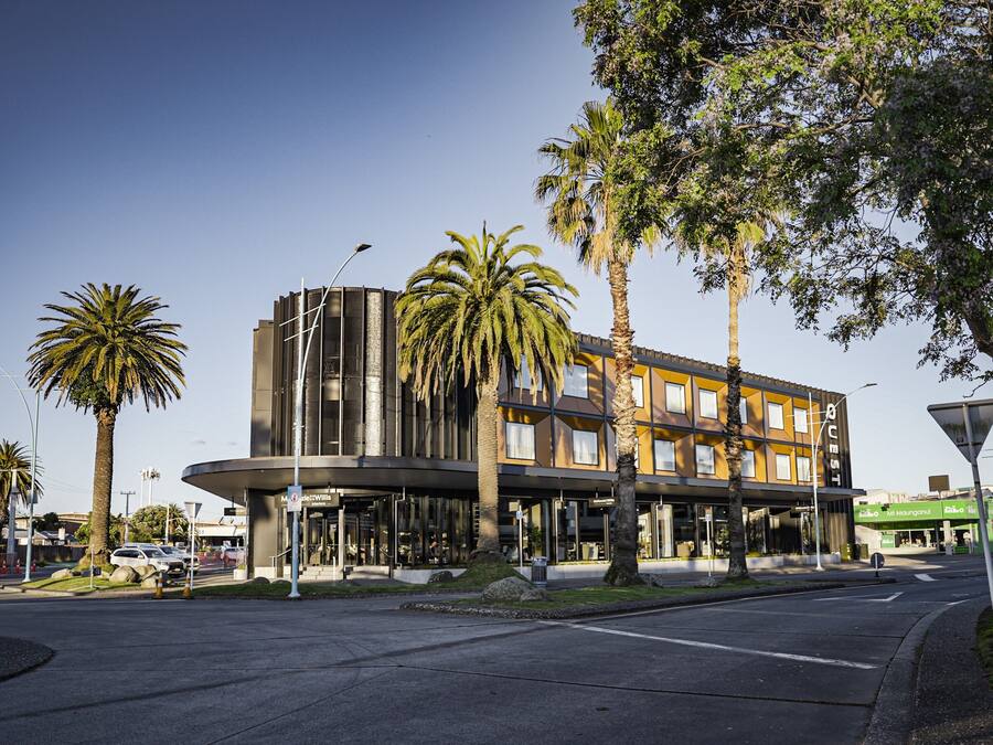 A modern hotel with a curved facade, palm trees, and a clear sky.