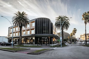 A modern hotel with a curved facade, palm trees, and a mountain in the background. - Quest Mt Maunganui  (Tauranga)