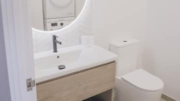A modern bathroom with a white sink, a mirror with a circular frame, a toilet, and a towel rack.