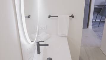 Een moderne badkamer met een witte wastafel, een spiegel met ingebouwde verlichting, een handdoekhouder en een zichtbare stopcontact.