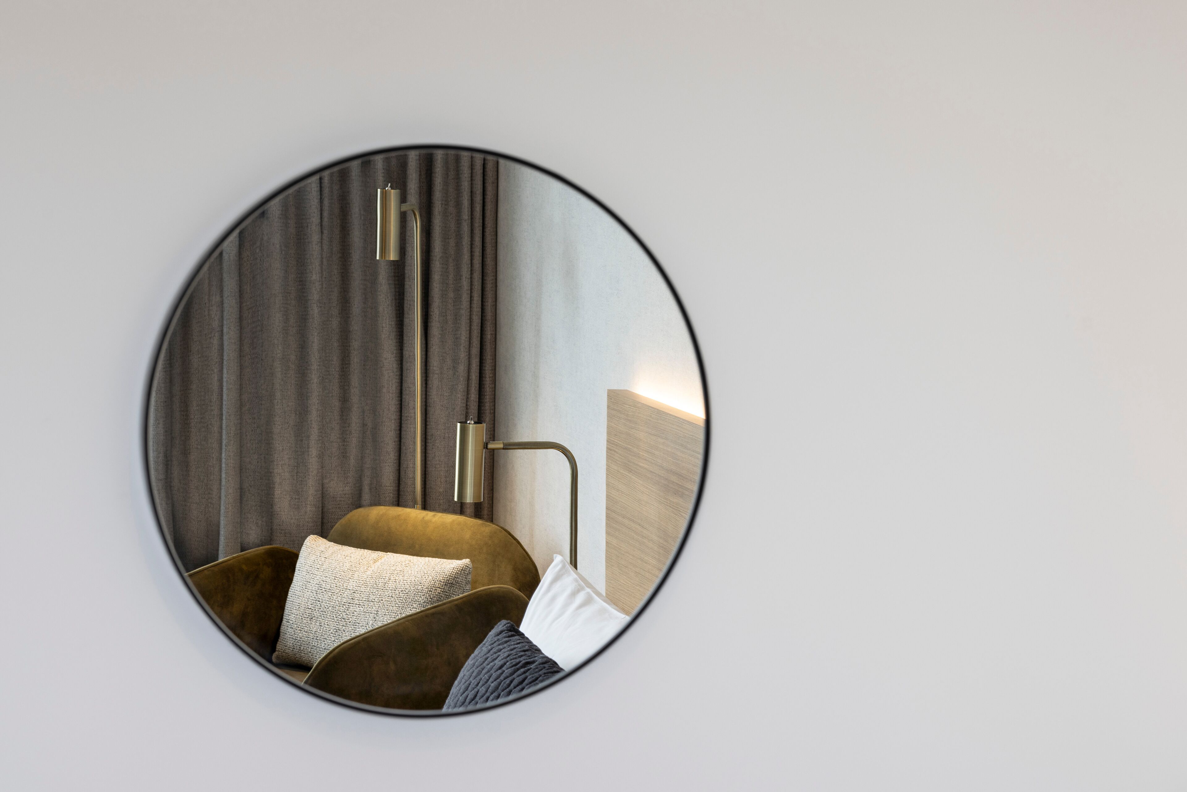 Un espejo redondo refleja una habitación moderna con un sofá, cojines y una lámpara de pared.