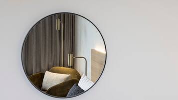 Un espejo redondo refleja una habitación moderna con un sofá, cojines y una lámpara de pared.