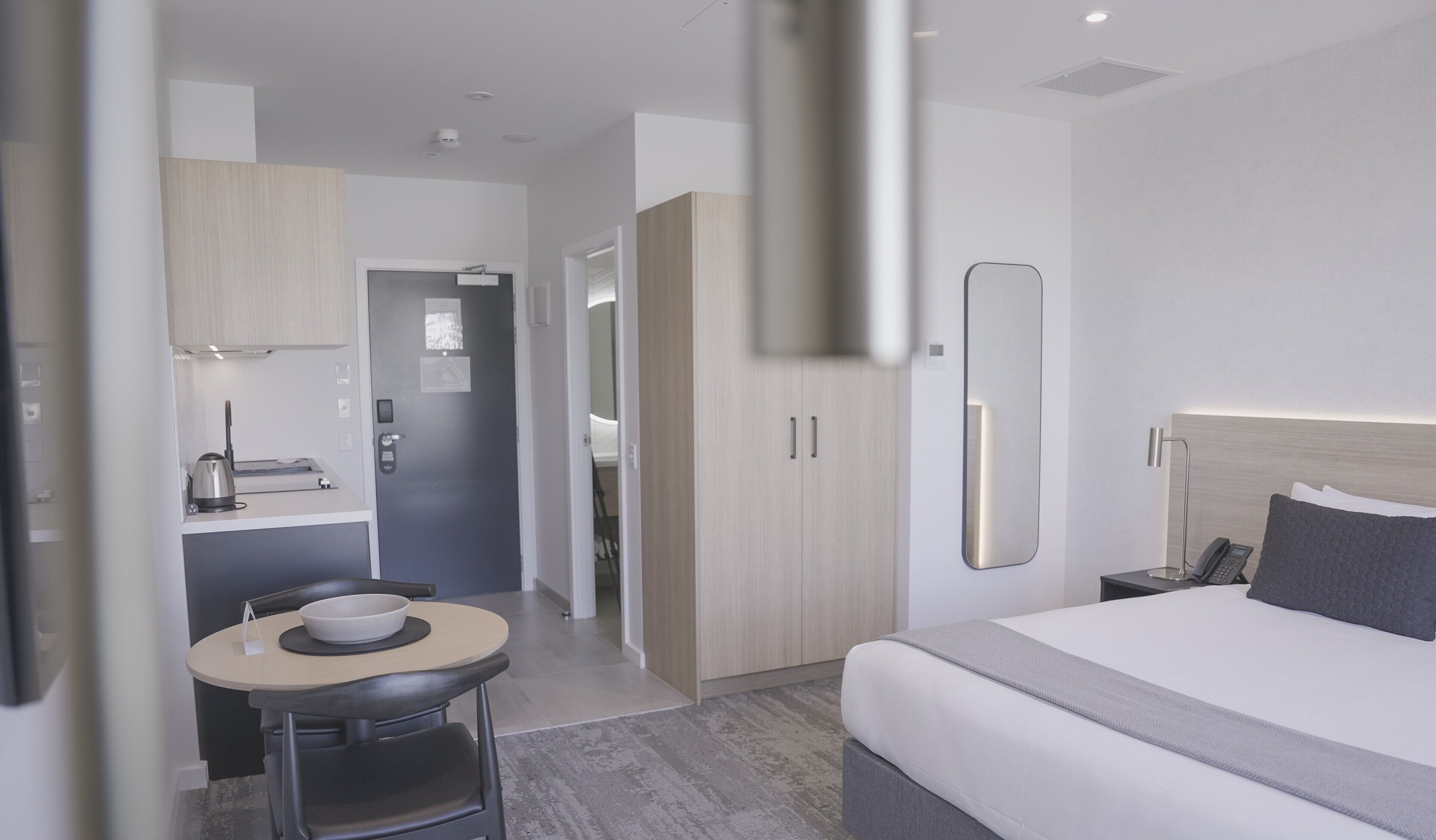 Hotellihuone, jossa on sänky, pieni pöytä ja kulho, tuoli, työpöytä, jossa on vedenkeitin, ja vaatekaappi.