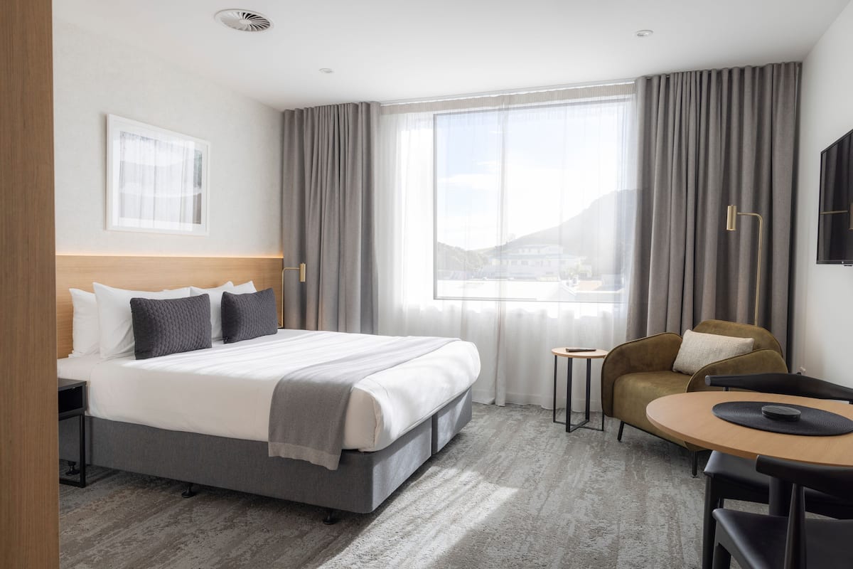 A modern hotel room with a large bed, a small round table, a sofa, and a view of the mountains through the window.