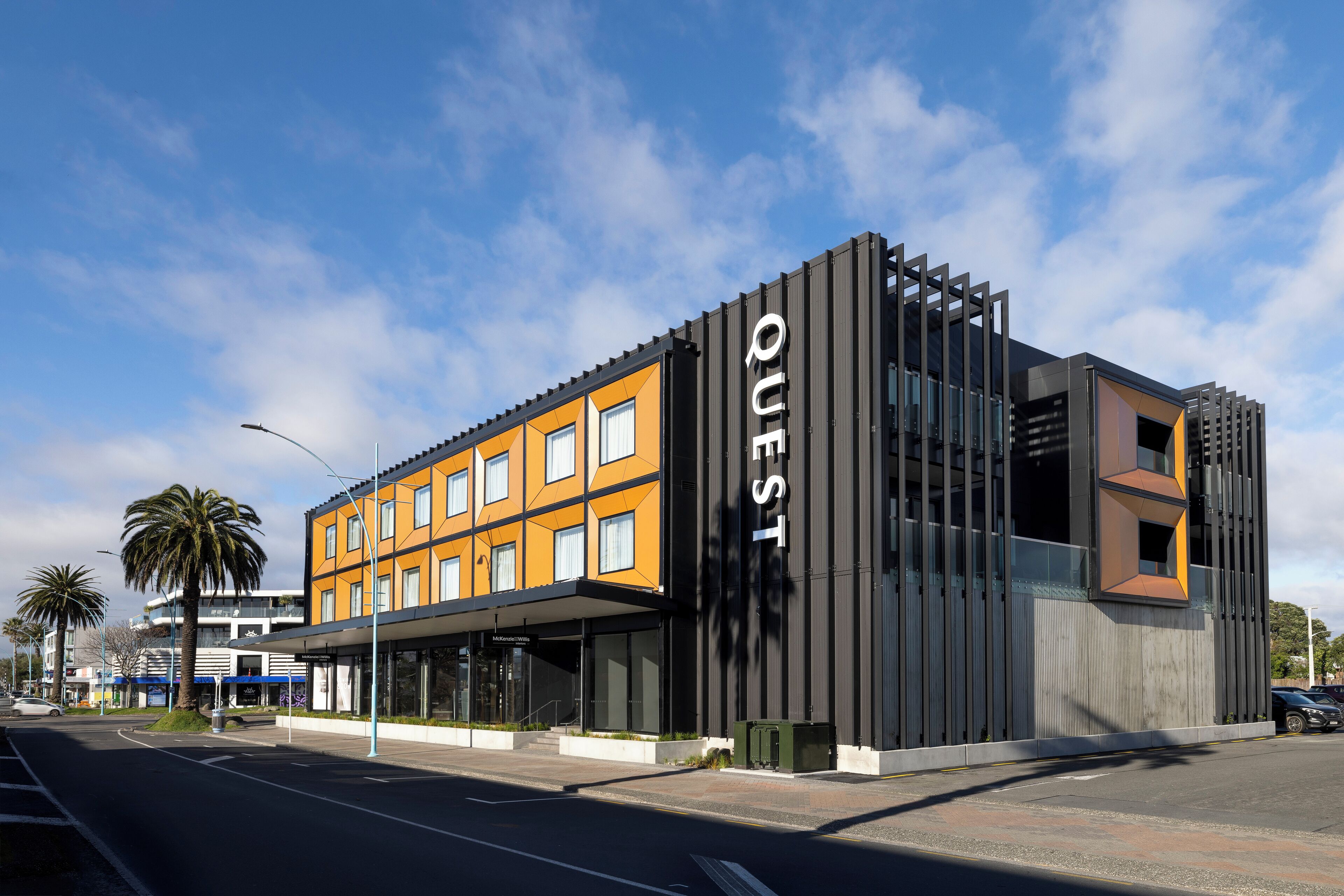 A modern building with a prominent "QUEST" sign, featuring a mix of glass and metal construction, and a flat-roof design.