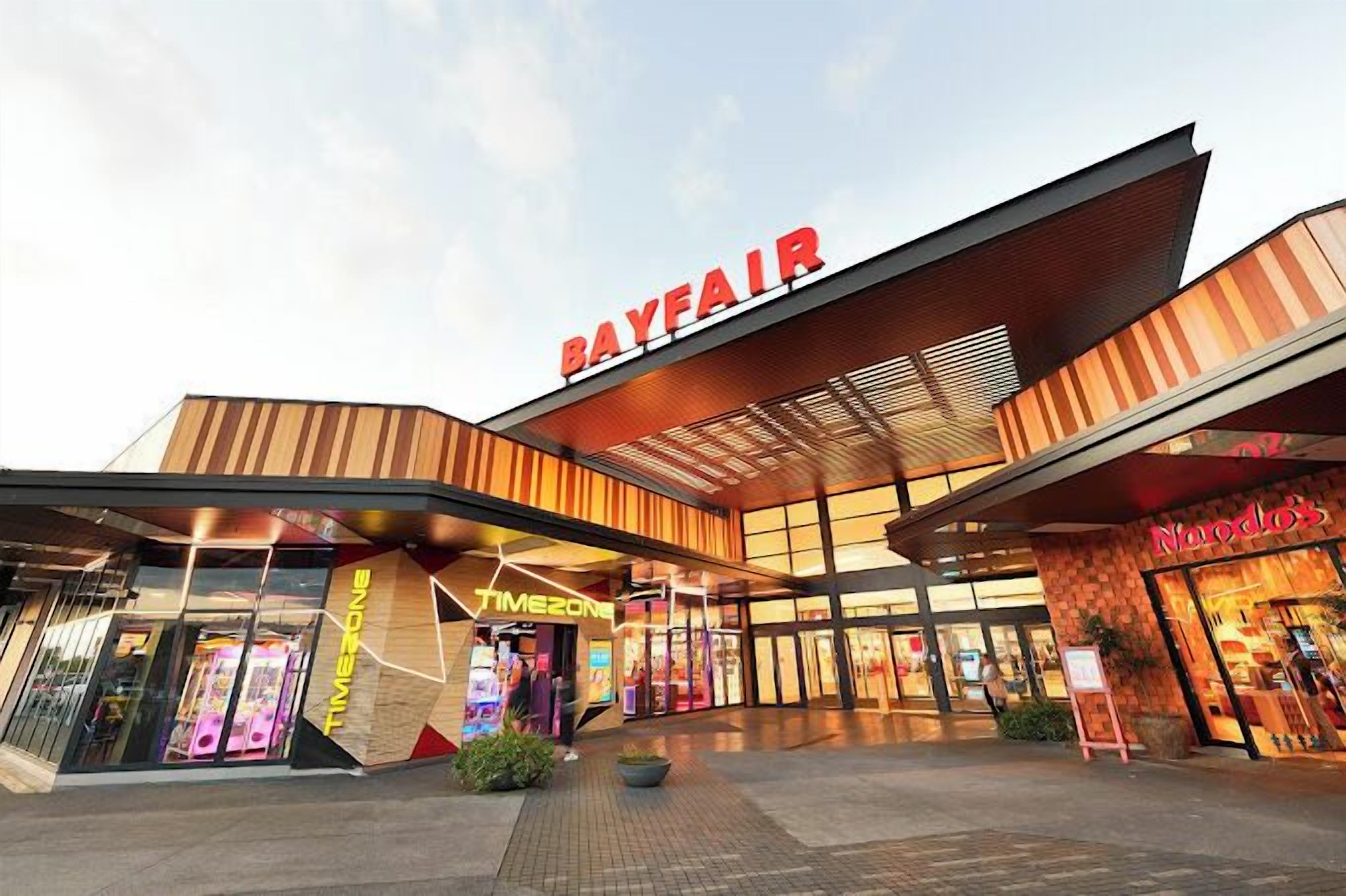 A modern building with a prominent 'Bayfair' sign, a 'Timezone' store, and a 'Noodles' restaurant.