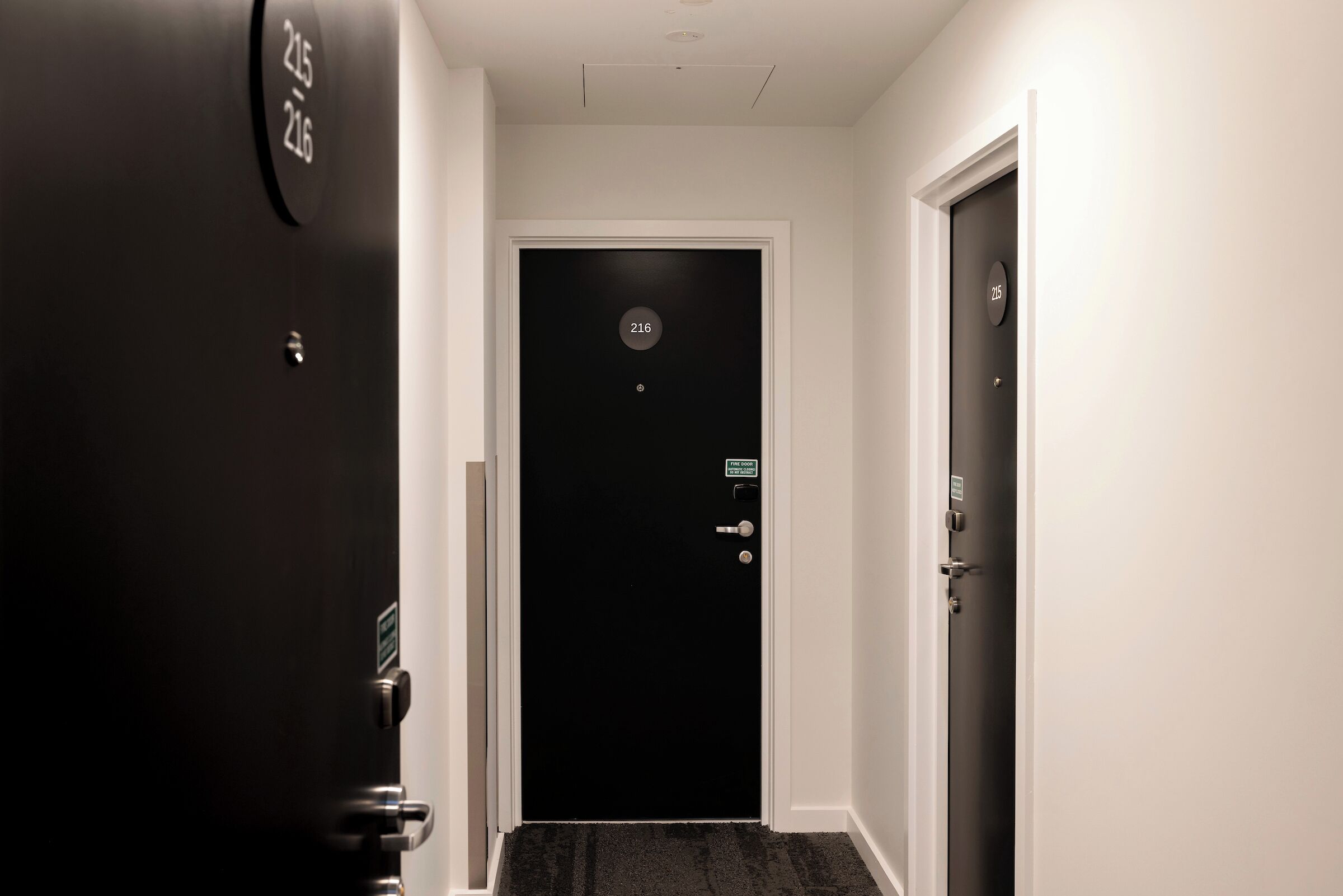 A hallway with a black door labeled 216, a doorbell, and a doorbell button.