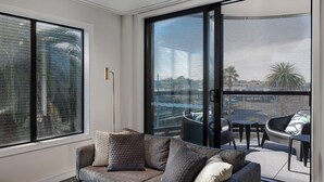 A modern living room with a grey sofa, a small table, and a balcony with a mesh screen. - Quest Mt Maunganui  (Tauranga)