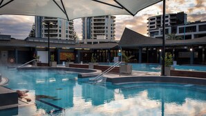 A swimming pool with a canopy, surrounded by modern buildings and a sunset sky. - Quest Mt Maunganui  (Tauranga)